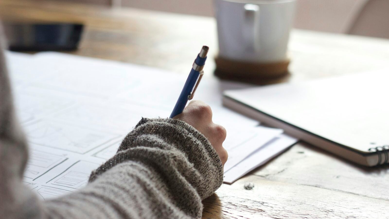 A student writing notes at a desk under a warm lamp late in the evening
