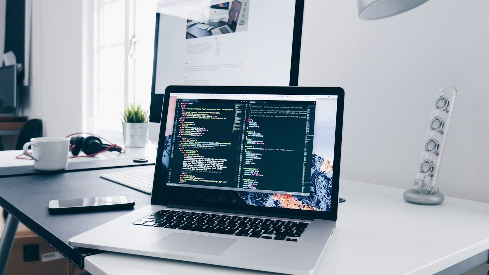 A laptop open on a desk beside a plant and a cup of coffee
